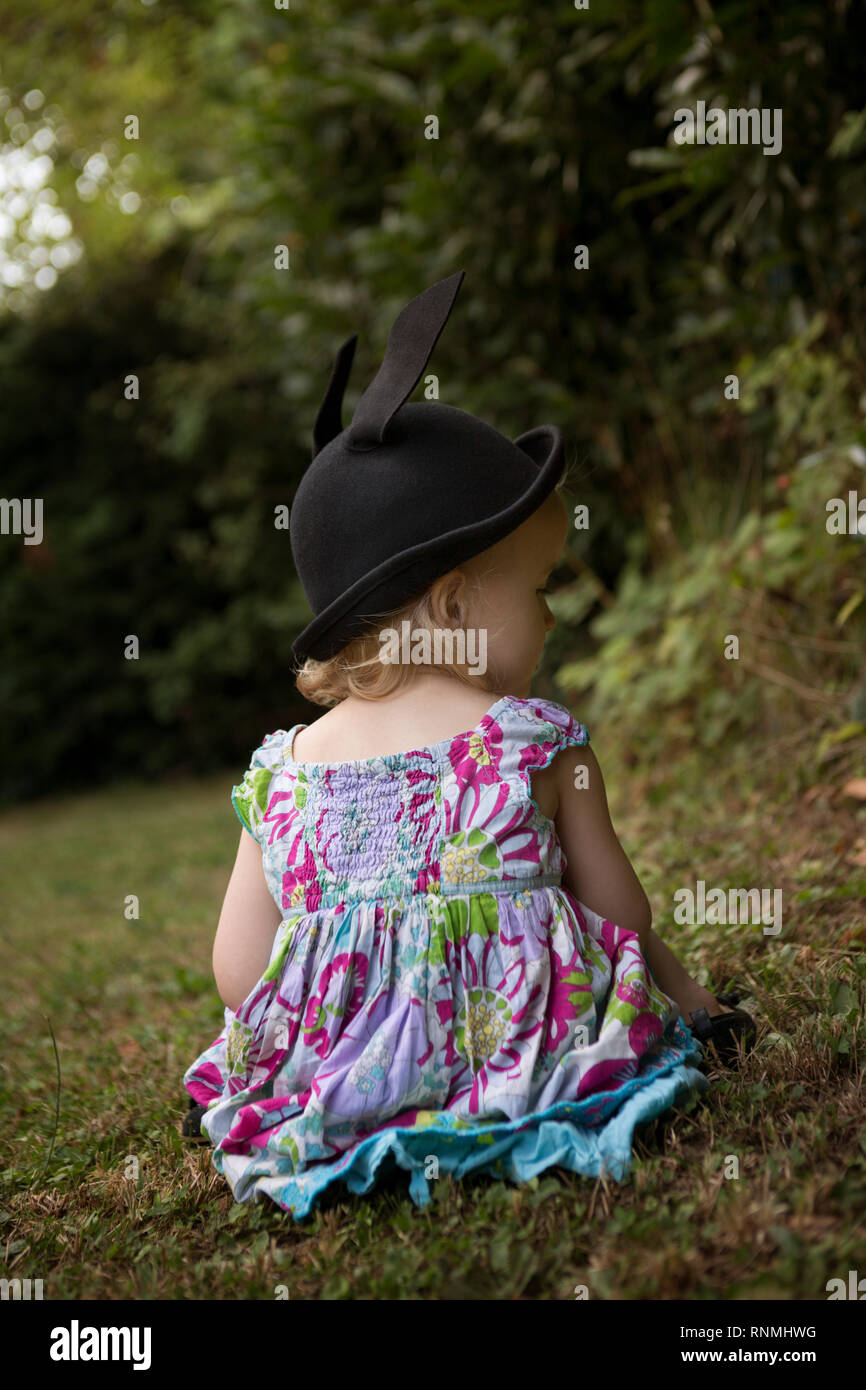 Vista posteriore del bambino seduto su erba, perso nel pensiero Foto Stock