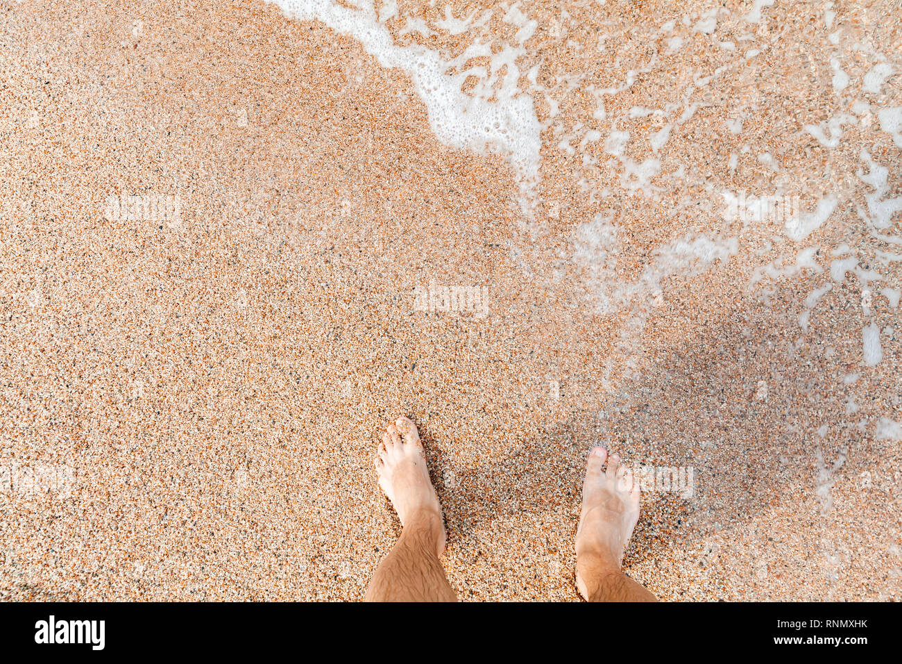 A piedi nudi le gambe di un uomo in piedi sulla sabbia costiera a giornata soleggiata, vista dall'alto Foto Stock