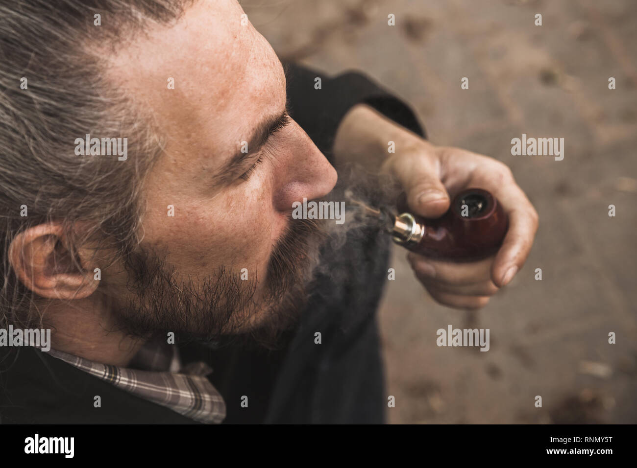 Brutale uomo barbuto tubazione di fumare in estate park, vicino la foto con il fuoco selettivo Foto Stock