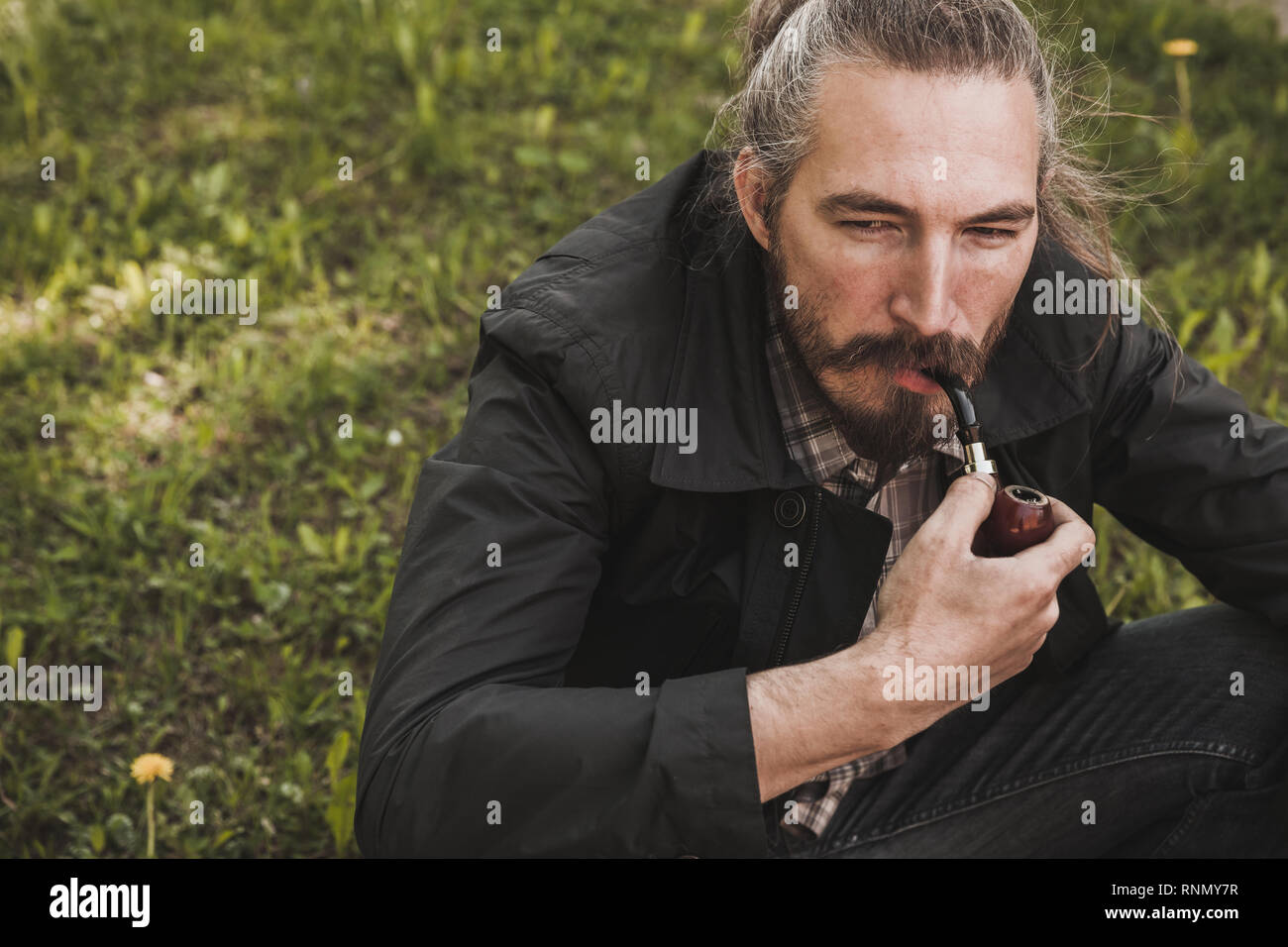 Grave uomo barbuto tubazione di fumare in estate park, vicino su ritratto Foto Stock