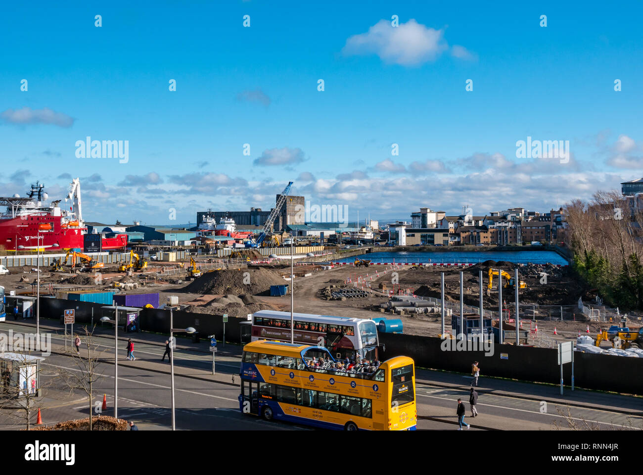 I lavori di costruzione sul sito di costruzione a Waterfront Plaza con i turisti in open top bus e navi in porto, Victoria Quay, Leith, Edimburgo, Scozia, Foto Stock