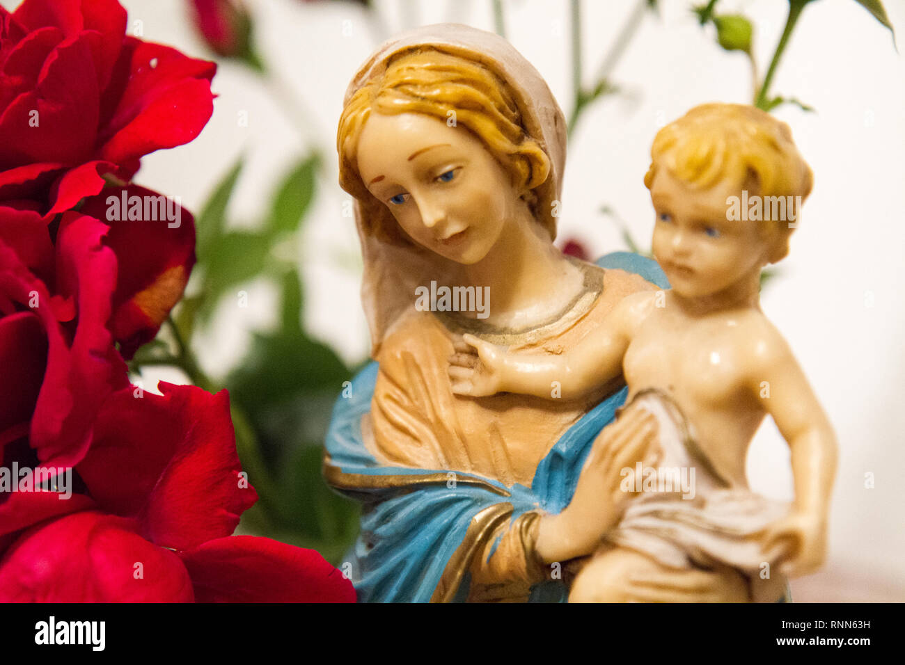 Una statua della Vergine Maria con il Bambino Gesù nelle sue braccia accanto a un mazzo di rose in una cappella. Foto Stock