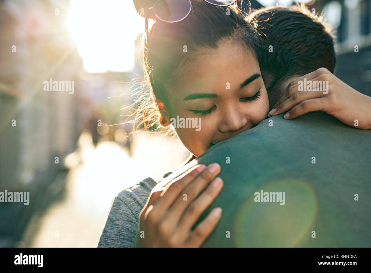 Giovane donna con gli occhi chiusi abbracciando il suo fidanzato mentre in piedi insieme su una strada di città nel tardo pomeriggio Foto Stock