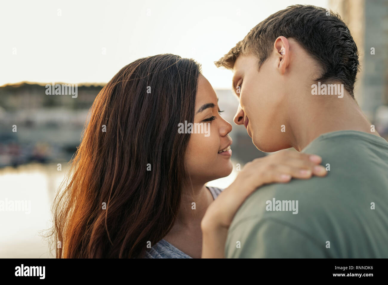 Affettuosa coppia giovane circa a baciare mentre in piedi a braccetto insieme da un porto nel tardo pomeriggio Foto Stock