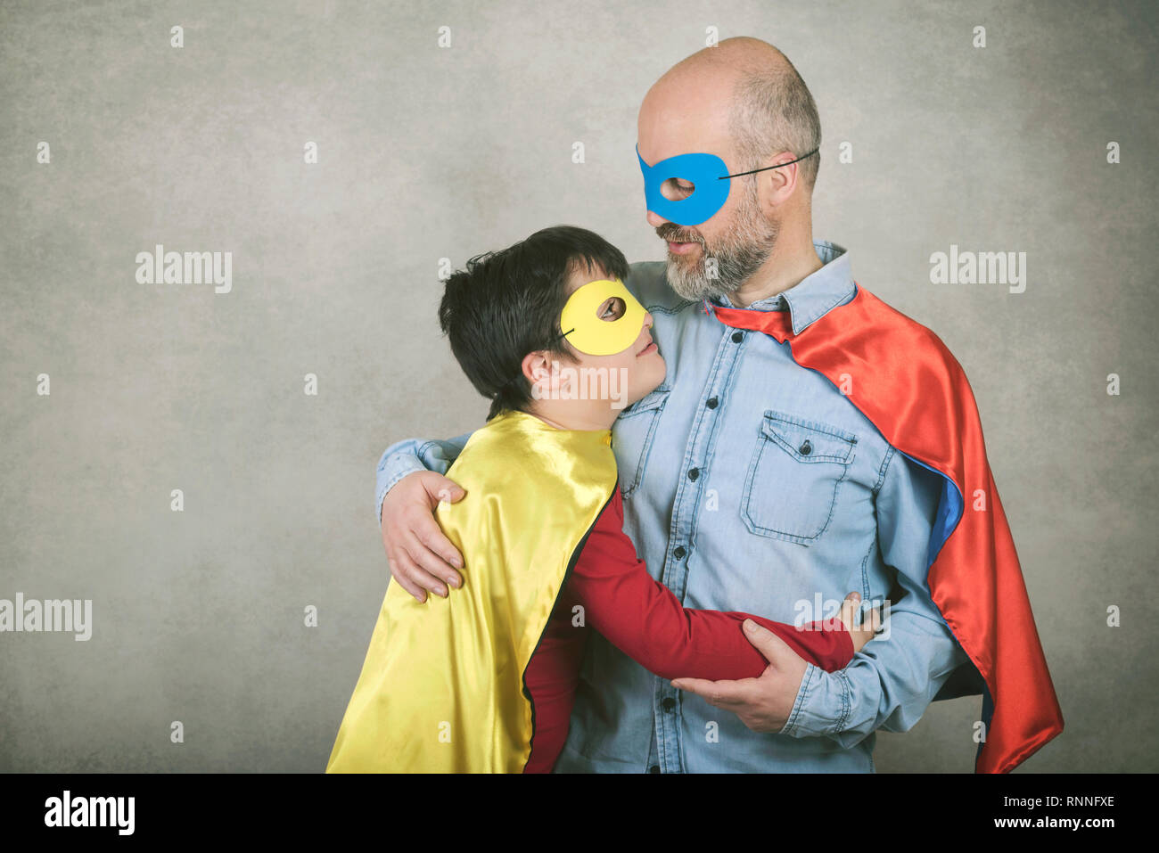 La festa del papà,padre e figlio vestito come un supereroe contro uno sfondo grigio Foto Stock