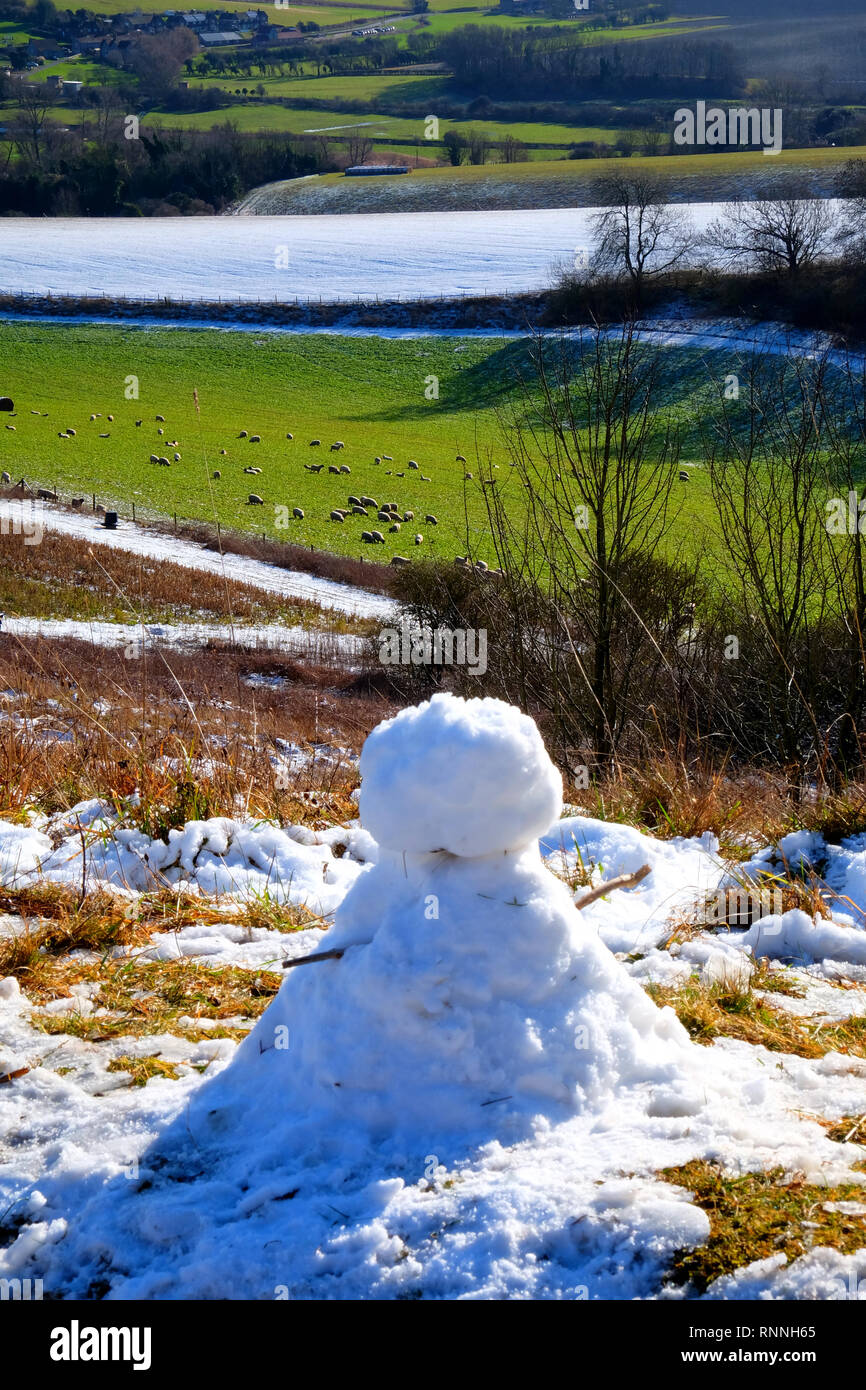 Un piccolo pupazzo di neve con bastoni come bracci si siede sul bordo della coperta di neve colline del South Downs national park, East Sussex, Regno Unito, il villaggio di G Foto Stock