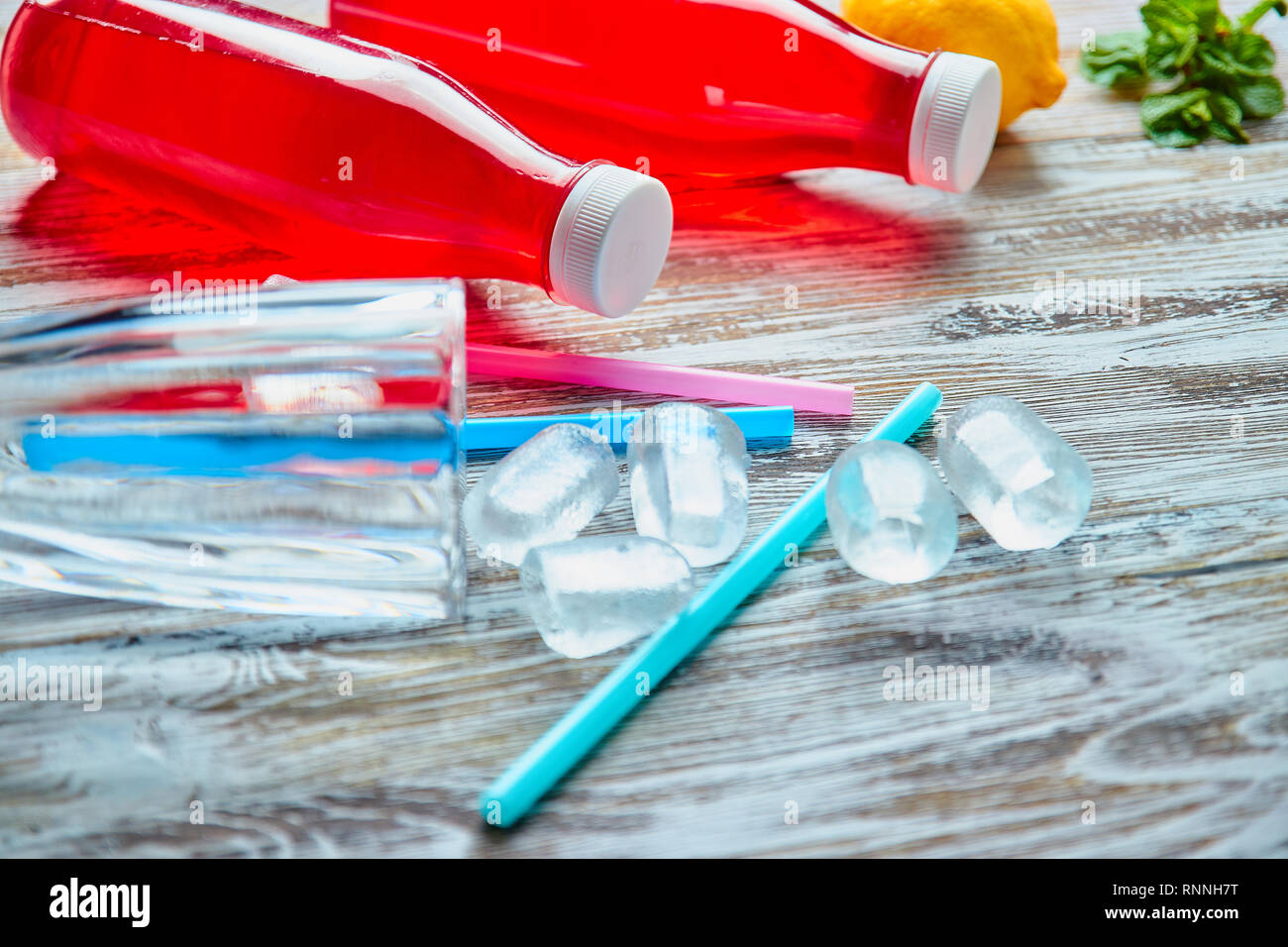Bottiglie di plastica con frutti di bosco, bevanda rinfrescante. sparsi di cubetti di ghiaccio e bere cannucce. Sullo sfondo di uno squallido tavolo in legno. close up. copia Foto Stock