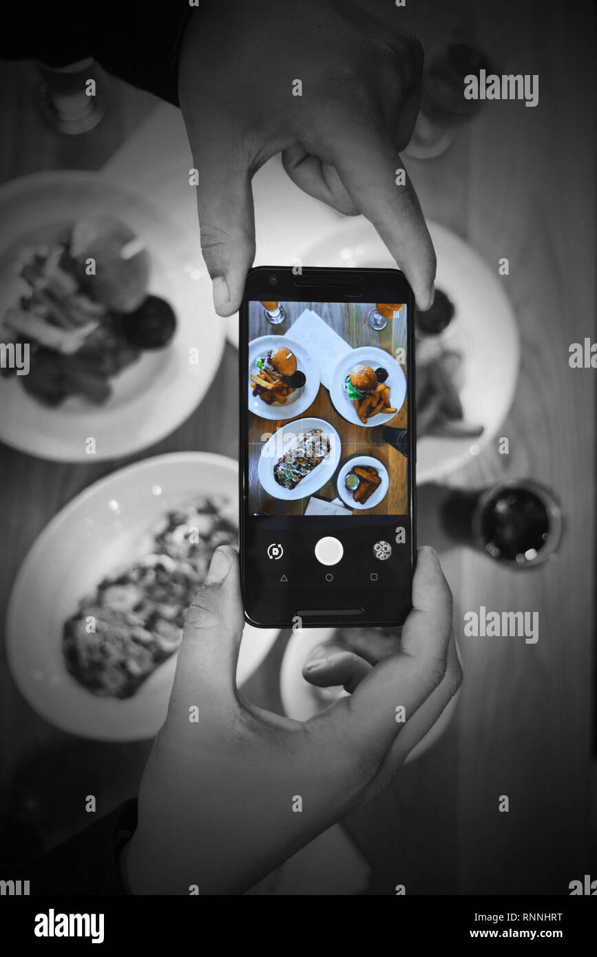 Maschio adulto mani prendendo una foto del loro pasto su una tabella con un telefono cellulare. La foto è presa dalla parte superiore del pasto. Foto Stock