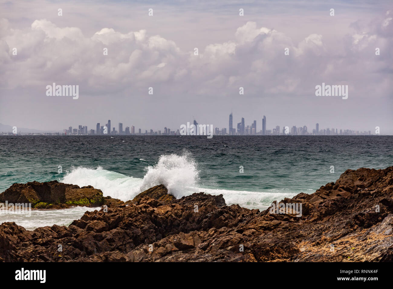 Oceano onde schiacciamento sul Snapper rocce con la Gold Coast skyline della città in background Foto Stock
