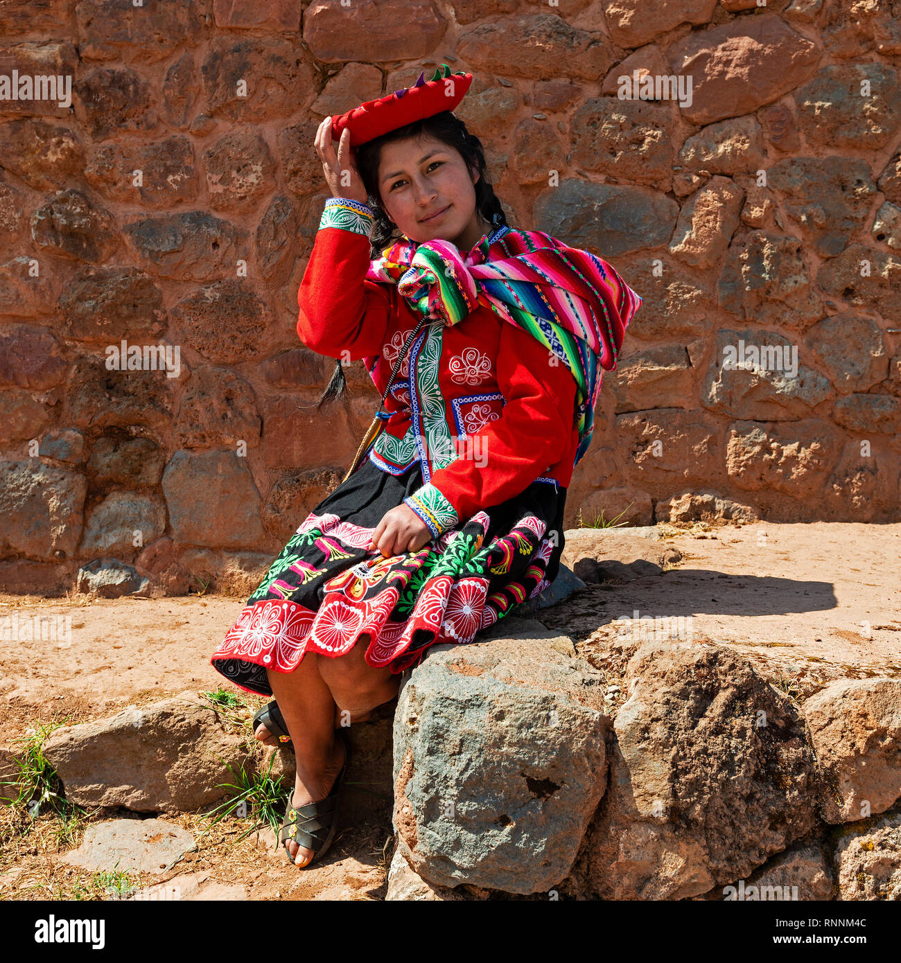 Giovani indigeni quechua ragazza in abiti tradizionali di fronte a un muro Inca del inca rovina Tipon vicino a Cusco, Perù. Foto Stock