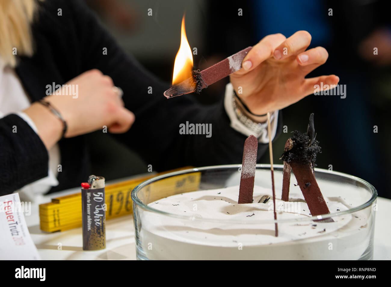 Il 20 febbraio 2019, il Land della Baviera, Norimberga: un dipendente di svt Brandschutz GmbH dimostra l'efficacia di una protezione antincendio rivestimento alla protezione antincendio congress 'Feuertrutz 2019'. Un bastone di legno, semi rivestiti con il prodotto è impostato sul fuoco sulla parte non rivestita. Il calore provoca la rivestimenti intumescenti a schiuma fino, impedendo così la propagazione del fuoco e di soffocare la fiamma. Foto: Daniel Karmann/dpa Foto Stock