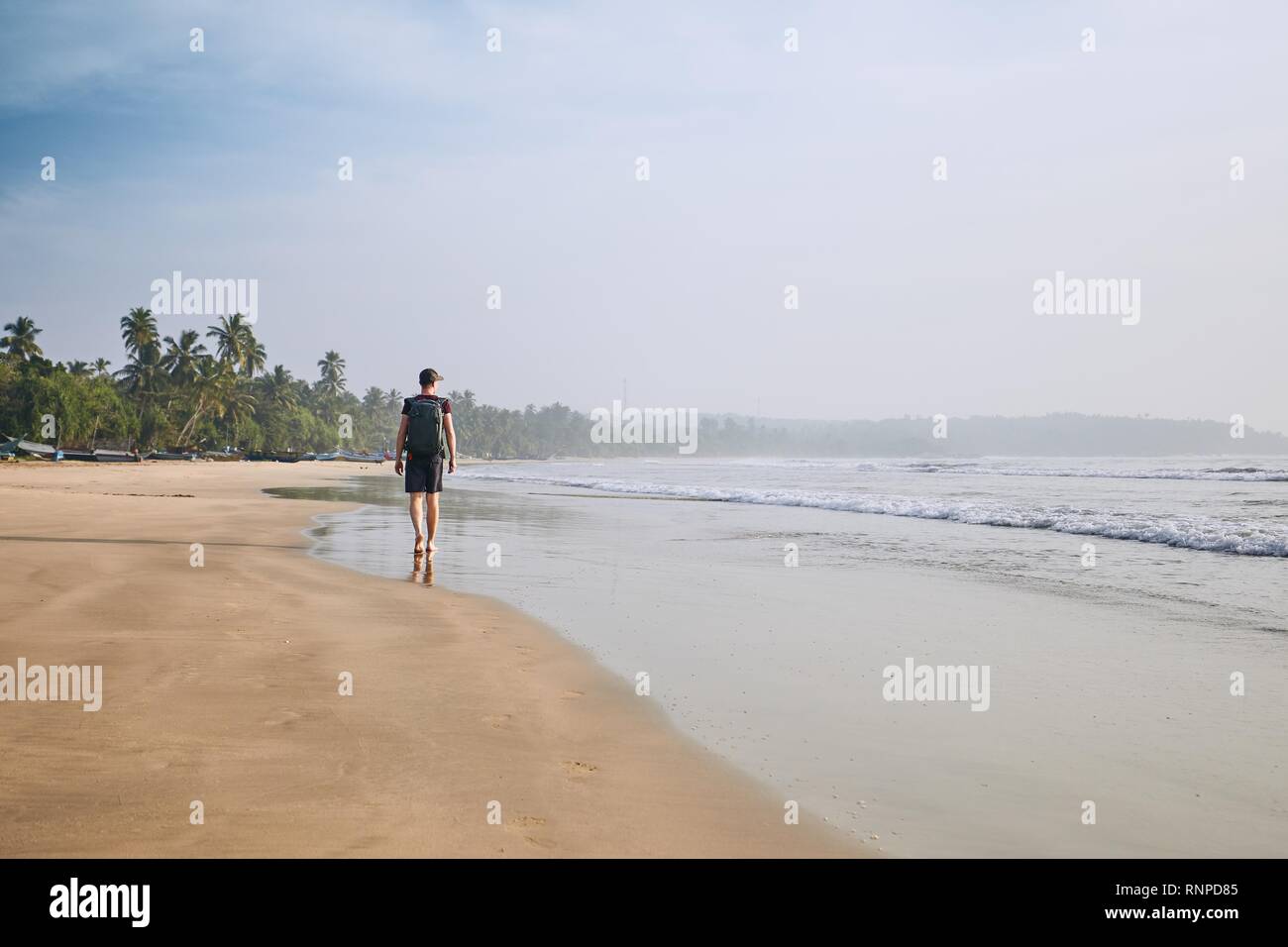 Giovane turista passeggiate sulla spiaggia di sabbia contro le palme. La costa vicino a Tangalle in Sri Lanka. Foto Stock
