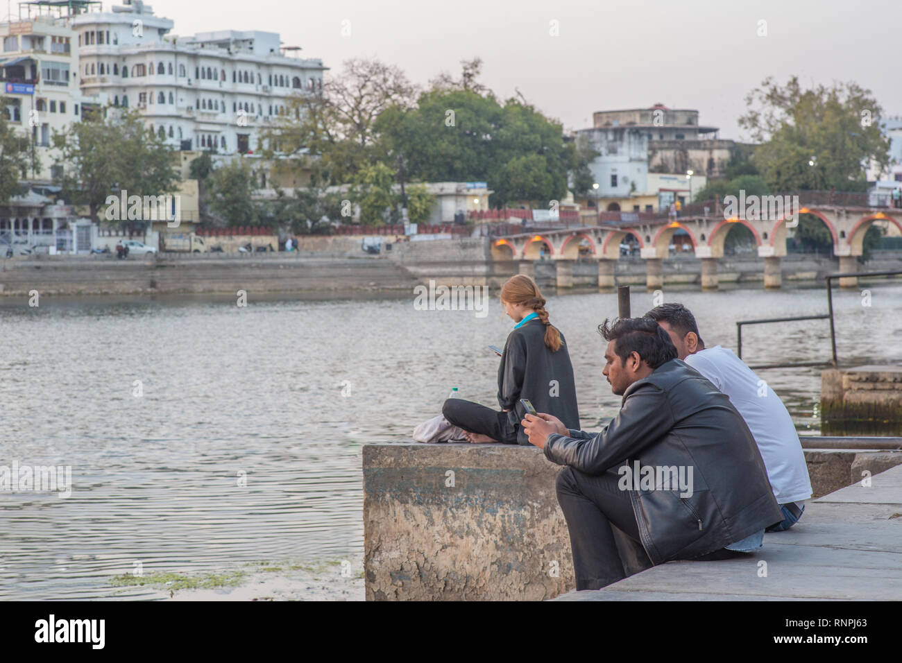 Un turista e alcuni locali utilizzando il proprio smartphone accanto a un lago nel Rajasthan, India Foto Stock