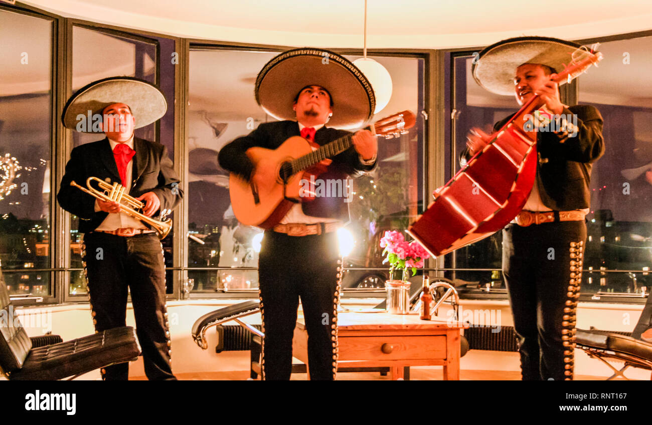 Scena in interni di un trio di mariachi messicani musicisti in costume tradizionale a un party privato, movimento sfocato Foto Stock