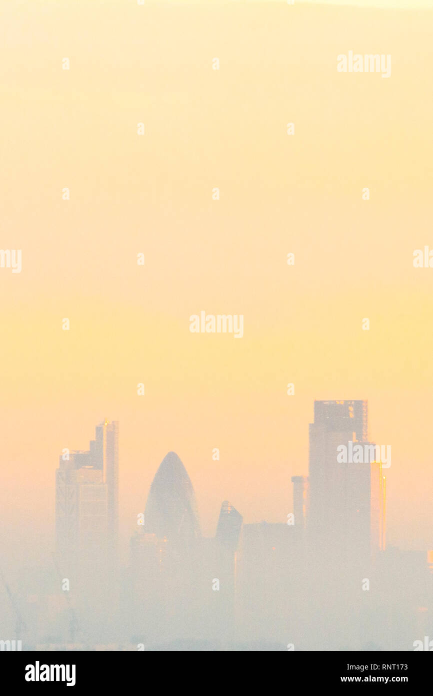 Edifici alti nella città di Londra, visto attraverso la nebbia e inquinamento nel bagliore dorato del tramonto Foto Stock