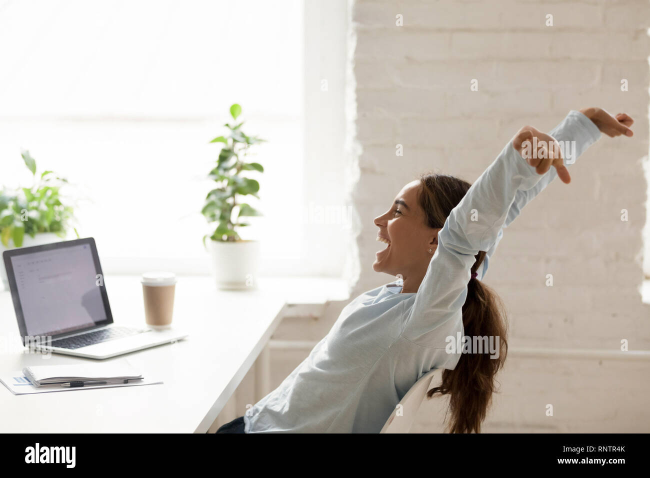Allegra donna stretching sollevando in alto le mani seduti al posto di lavoro Foto Stock