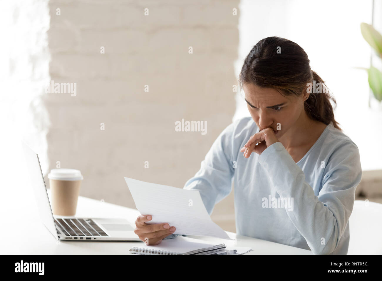 Frustrati giovane donna seduta a tavola lettura la lettera Foto Stock