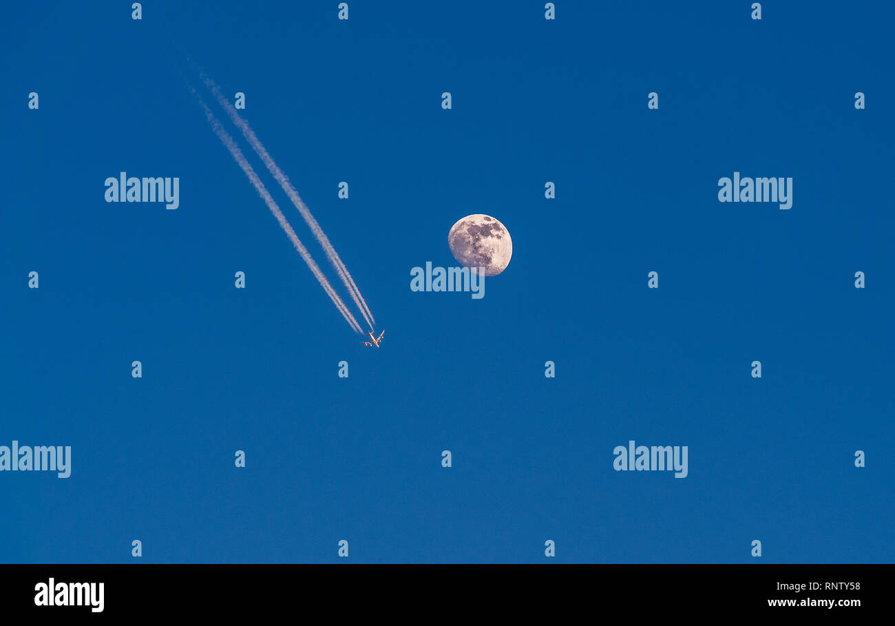 Immagine del velivolo con le scie di condensazione battenti accanto alla dettagliata luna con cielo blu Foto Stock