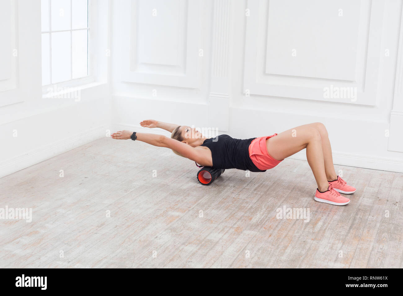 Bella athletic giovane donna nel quartiere alla moda di montare l'usura utilizzando il rullo di schiuma in palestra di allenamento per rimuovere il dolore alla schiena, stretching e massaggiare muscoli. Reha Foto Stock