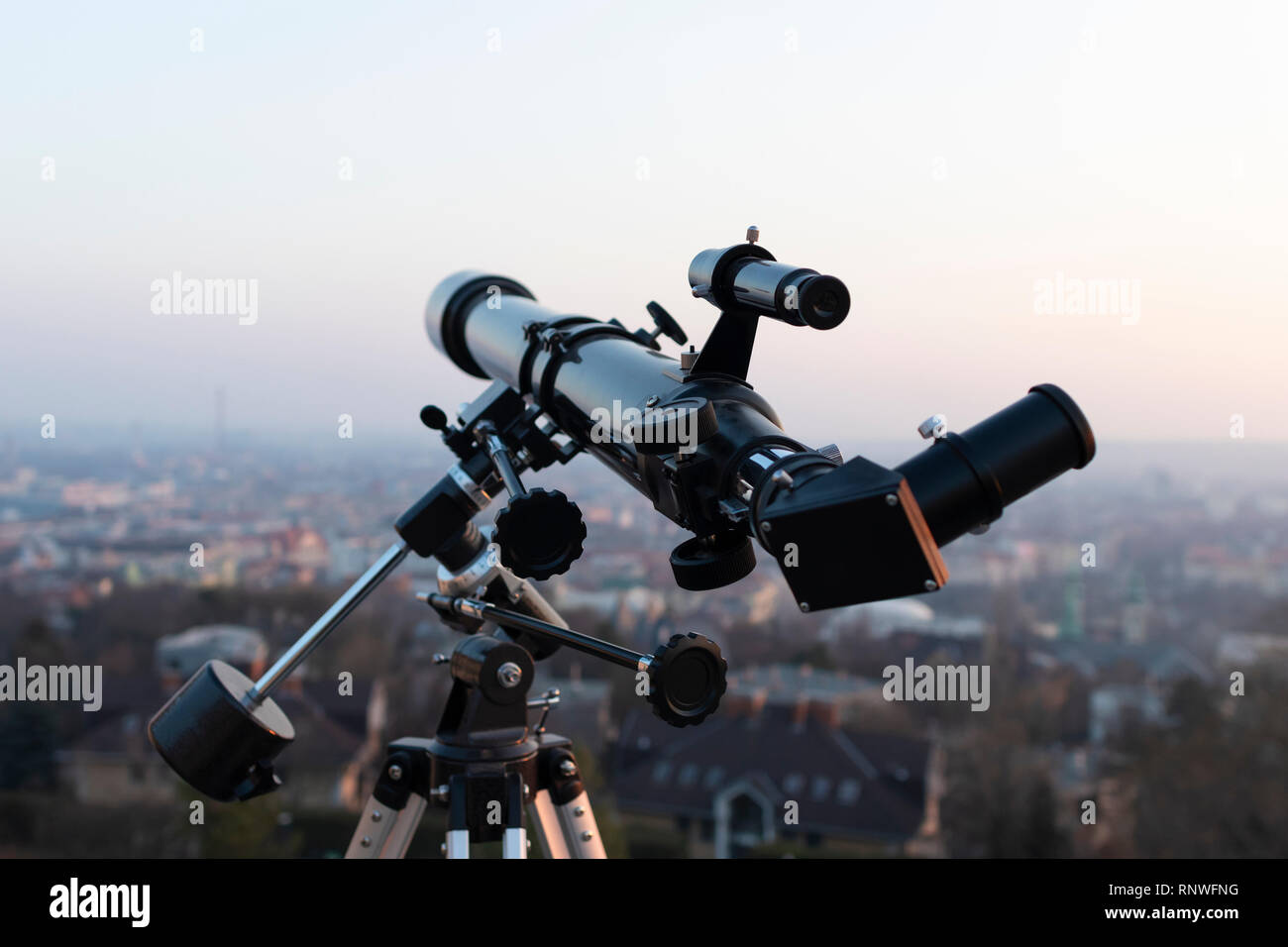 Un professionista di telescopio rifrattore montato su un treppiede, guardando una grande città al tramonto Foto Stock