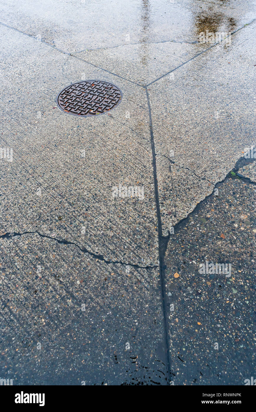 Un particolare colpo di un calcestruzzo street e un chiusino durante una tempesta di pioggia. Foto Stock