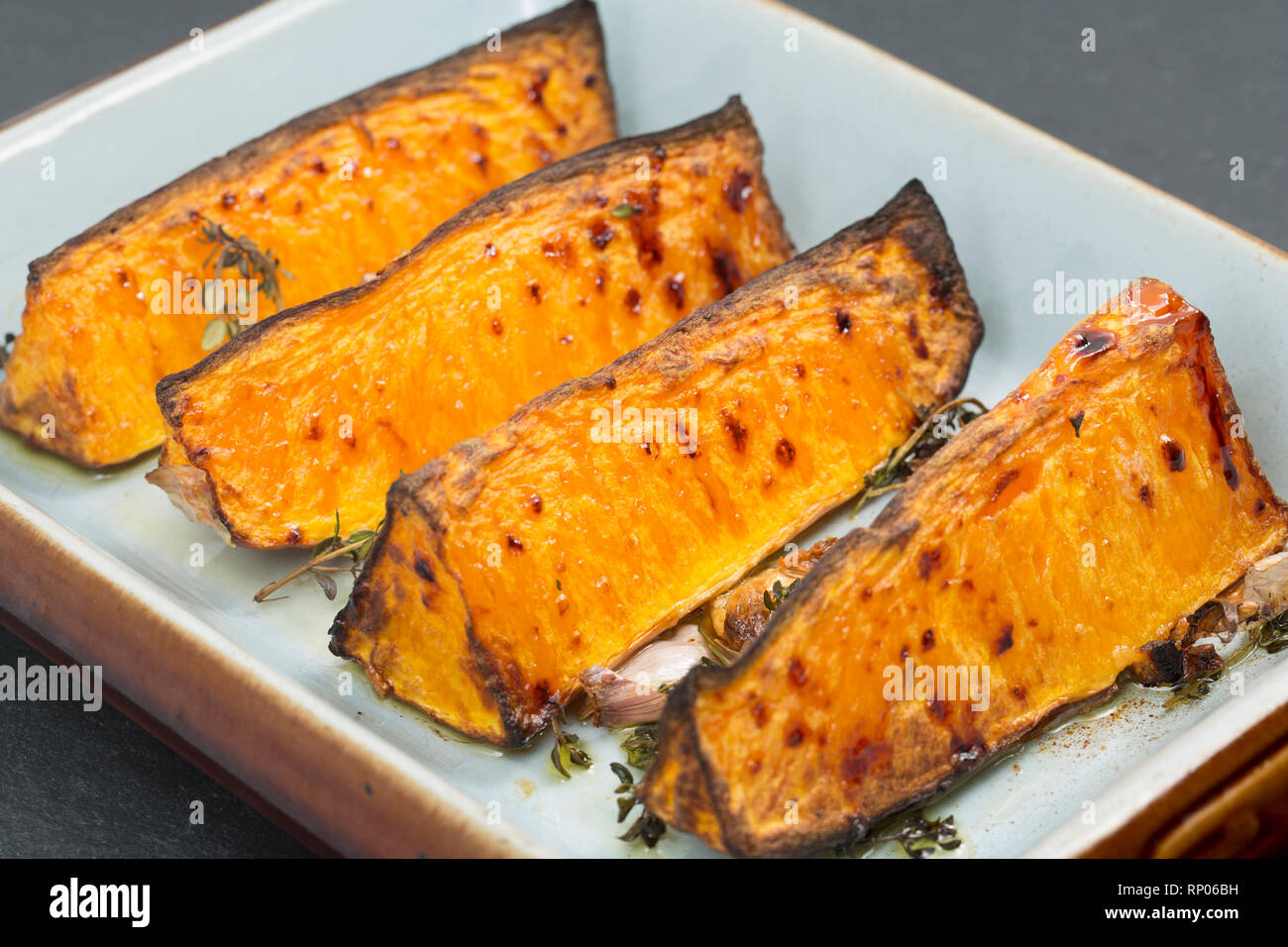 Quattro spicchi di zucca con la pelle a sinistra su acquistato da un supermercato che sono state tostate in forno con olio d'oliva, aglio schiacciato e Foto Stock