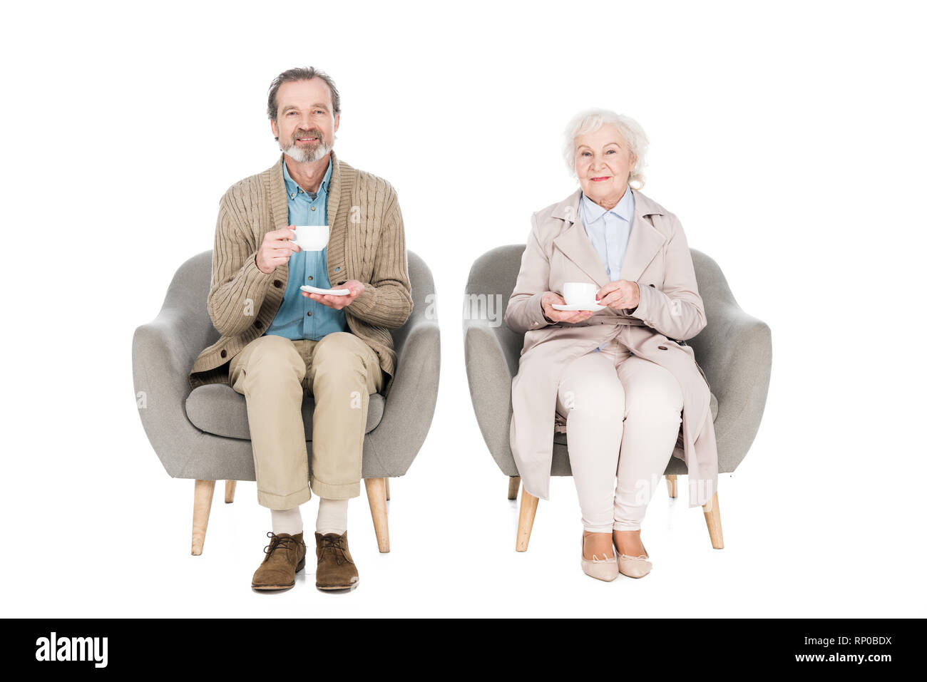 Felice coppia senior poggiarvi bicchieri con tè mentre è seduto in poltrona isolato su bianco Foto Stock