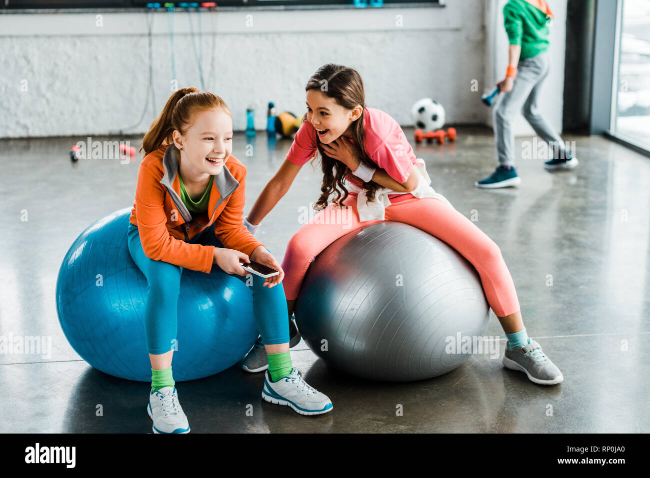Ridere i bambini con lo smartphone seduti sulle sfere di fitness Foto Stock