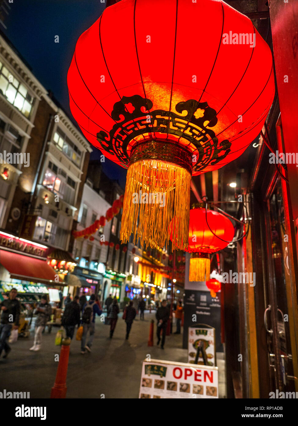 Le lanterne cinesi illuminato in primo piano al di fuori di ristoranti cinesi con i visitatori dietro a Gerrard Street in una trafficata shopping e ristoranti di notte in Chinatown Soho London REGNO UNITO Foto Stock
