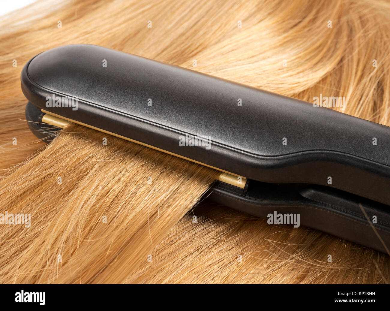 La raddrizzatura lunghi capelli biondi capelli con il ferro da stiro Foto Stock
