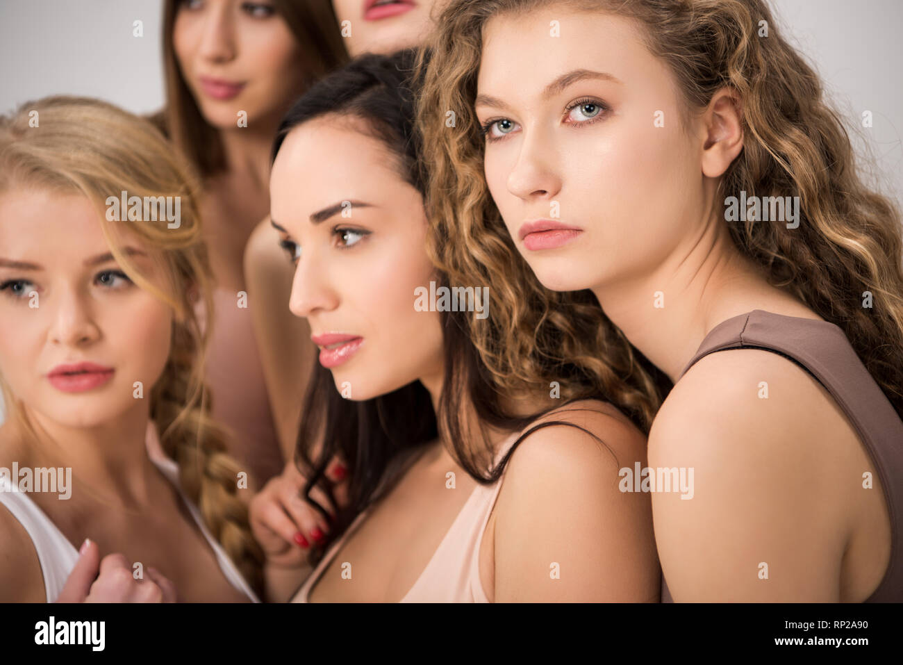 Messa a fuoco selettiva di donne attraenti in piedi insieme mentre si sostengono reciprocamente isolati su grigio Foto Stock