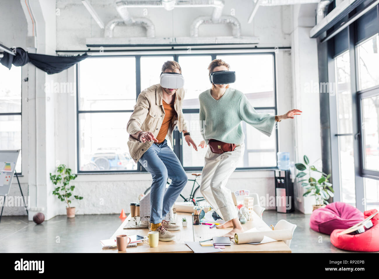 Maschi e femmine di architetti indossando le cuffie vr, gesti con le mani e aventi esperienza virtuale in ufficio loft Foto Stock