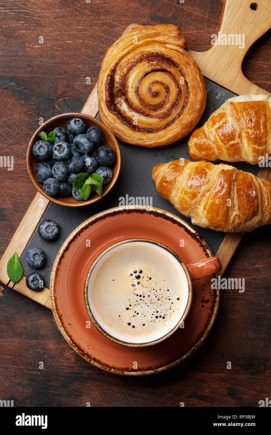 Caffè, cornetti, panini alla cannella e le bacche di prima colazione. Sul tavolo di legno Foto Stock