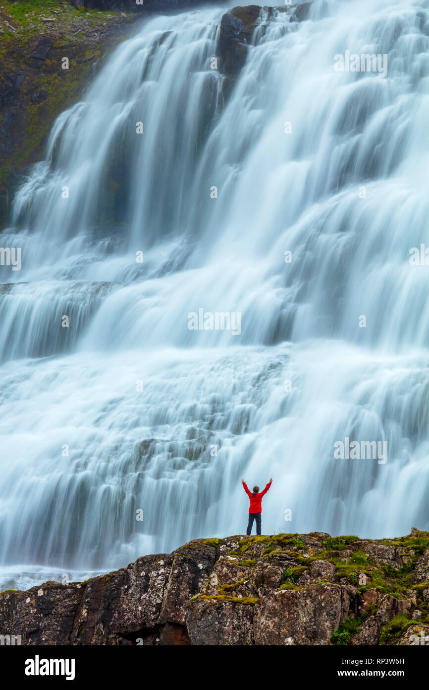 Persona sopraffatte dalla cascata Dynjandi o Fjallfoss, Westfjords, Islanda. Foto Stock