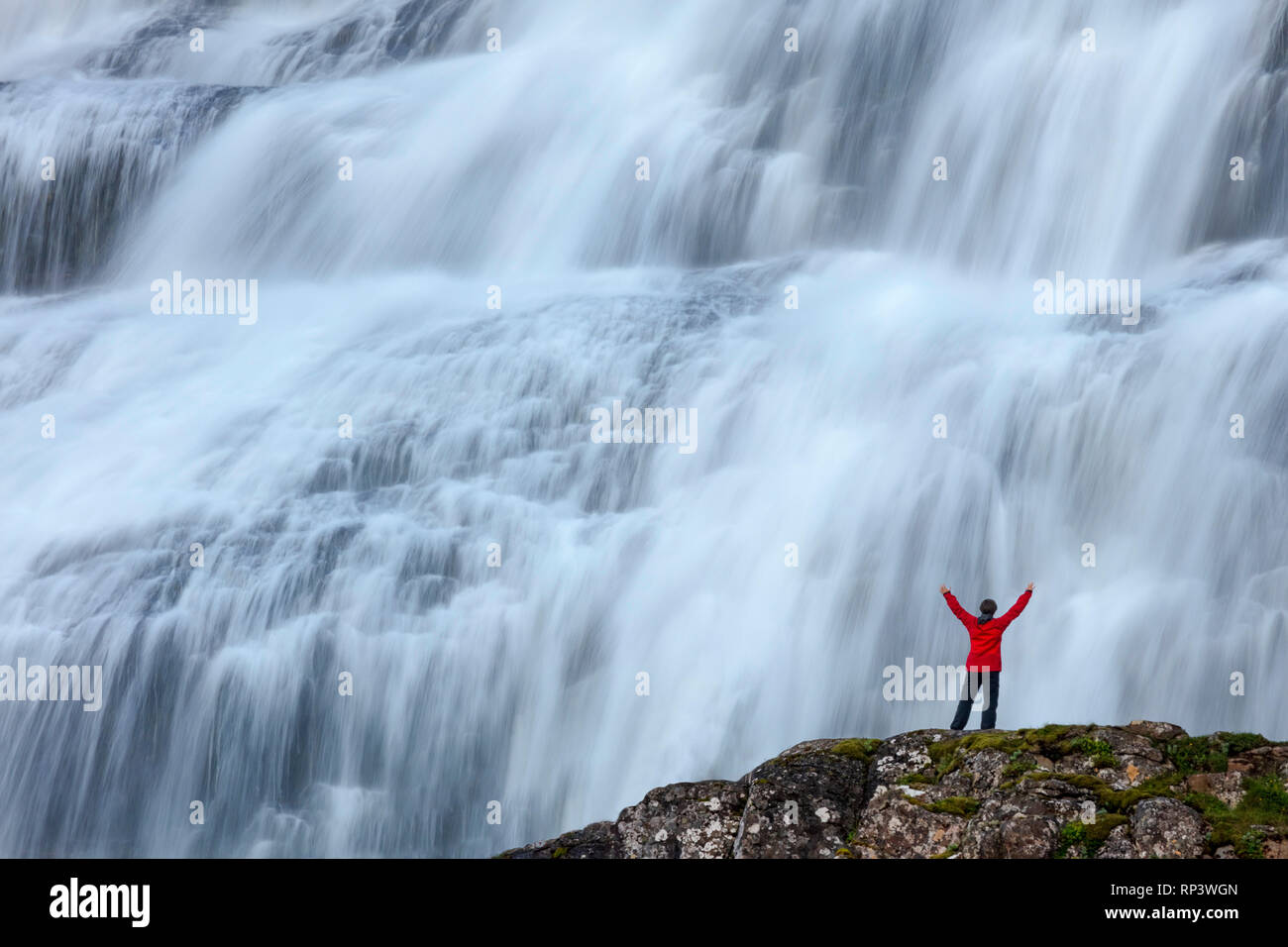 Persona sopraffatte dalla cascata Dynjandi o Fjallfoss, Westfjords, Islanda. Foto Stock