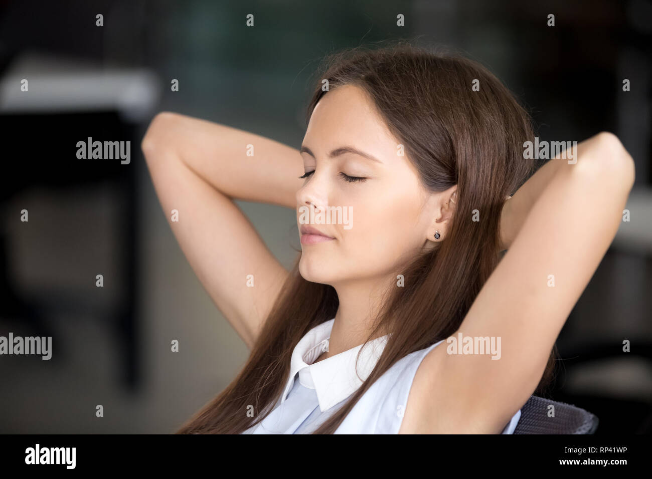 Close up da solo femmina con gli occhi chiusi a sognare seduto in ufficio dopo il lavoro tenendo le mani dietro la testa. Studente o dipendente respirando aria fresca si sente Foto Stock