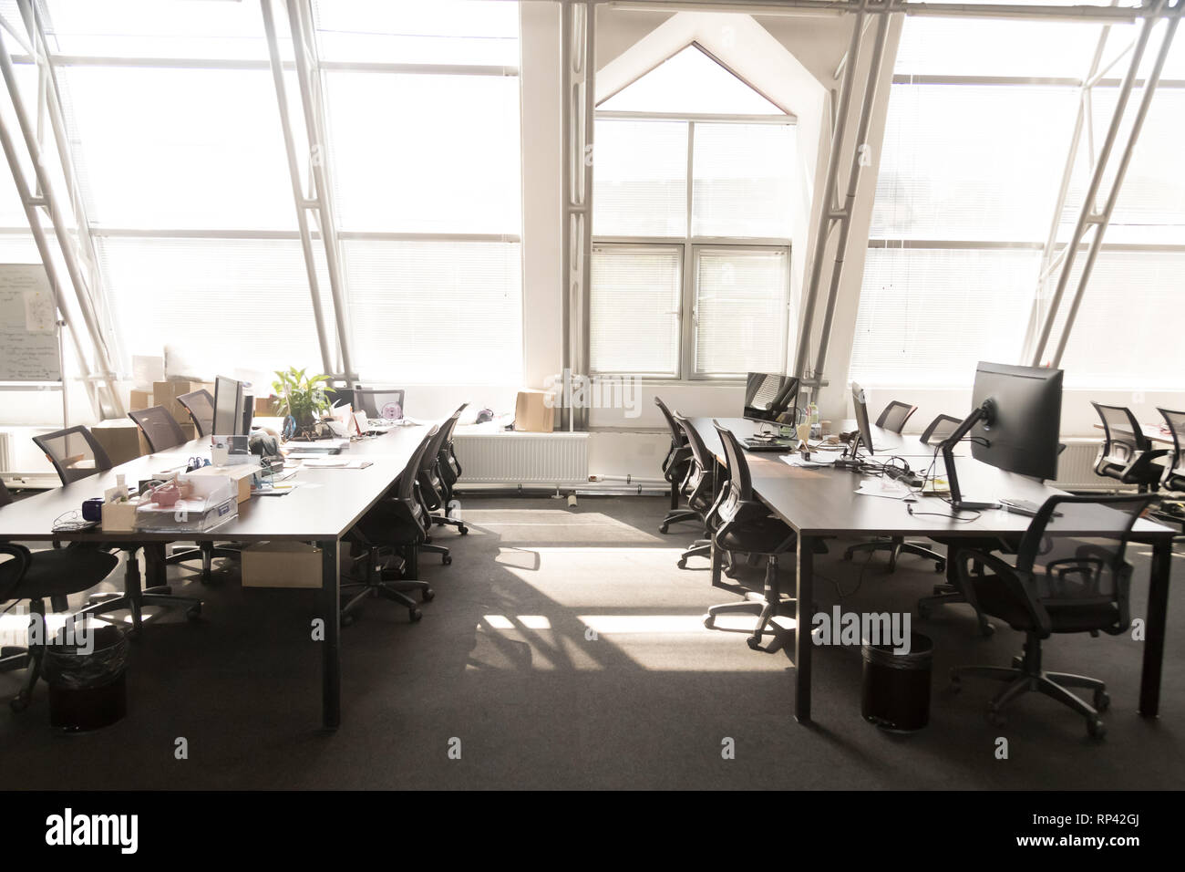Luce moderno spazioso ufficio sala interna. Computer su tavoli sedie nere su ruote, la luce del sole attraverso le finestre panoramiche. Confortevole contempora Foto Stock