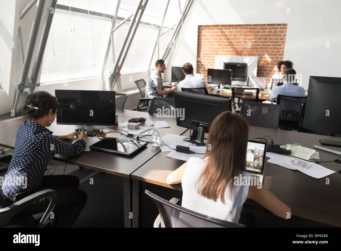 Diversi dipendenti millenaria maschio femmina seduto alla scrivania con computer portatili che lavorano in coworking spazio aperto moderna e luminosa camera con finestre panoramiche. Multi Foto Stock