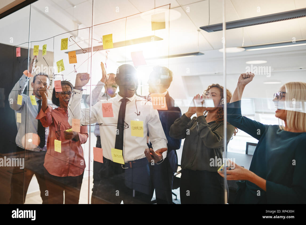 Diversi gruppi di imprenditori estatica celebrando e alta fiving insieme durante il brainstorming su una parete di vetro in un ufficio moderno Foto Stock