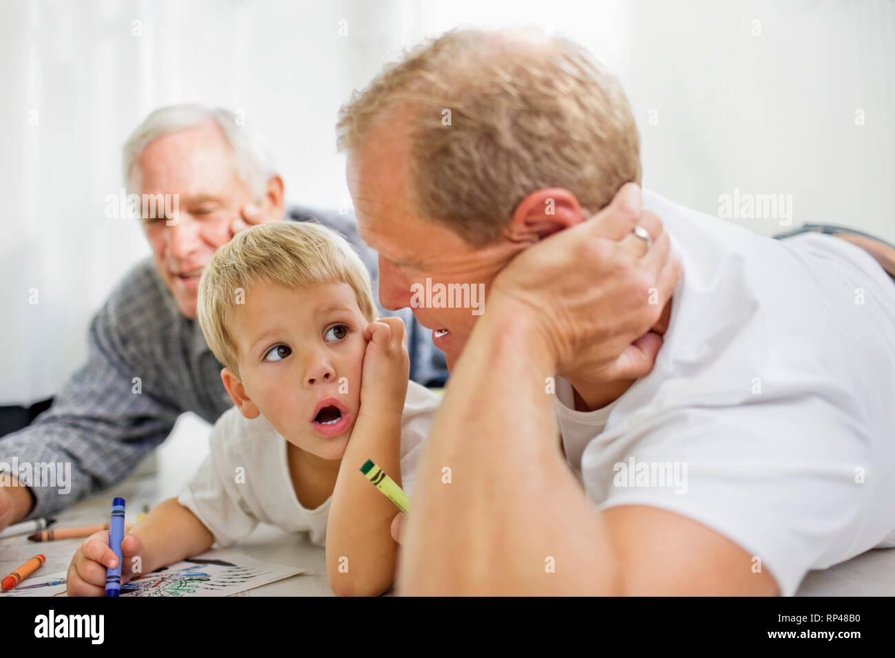 Ragazzo con la sua metà adulto padre e nonno maturo sdraiato sul pavimento a colorare. Foto Stock