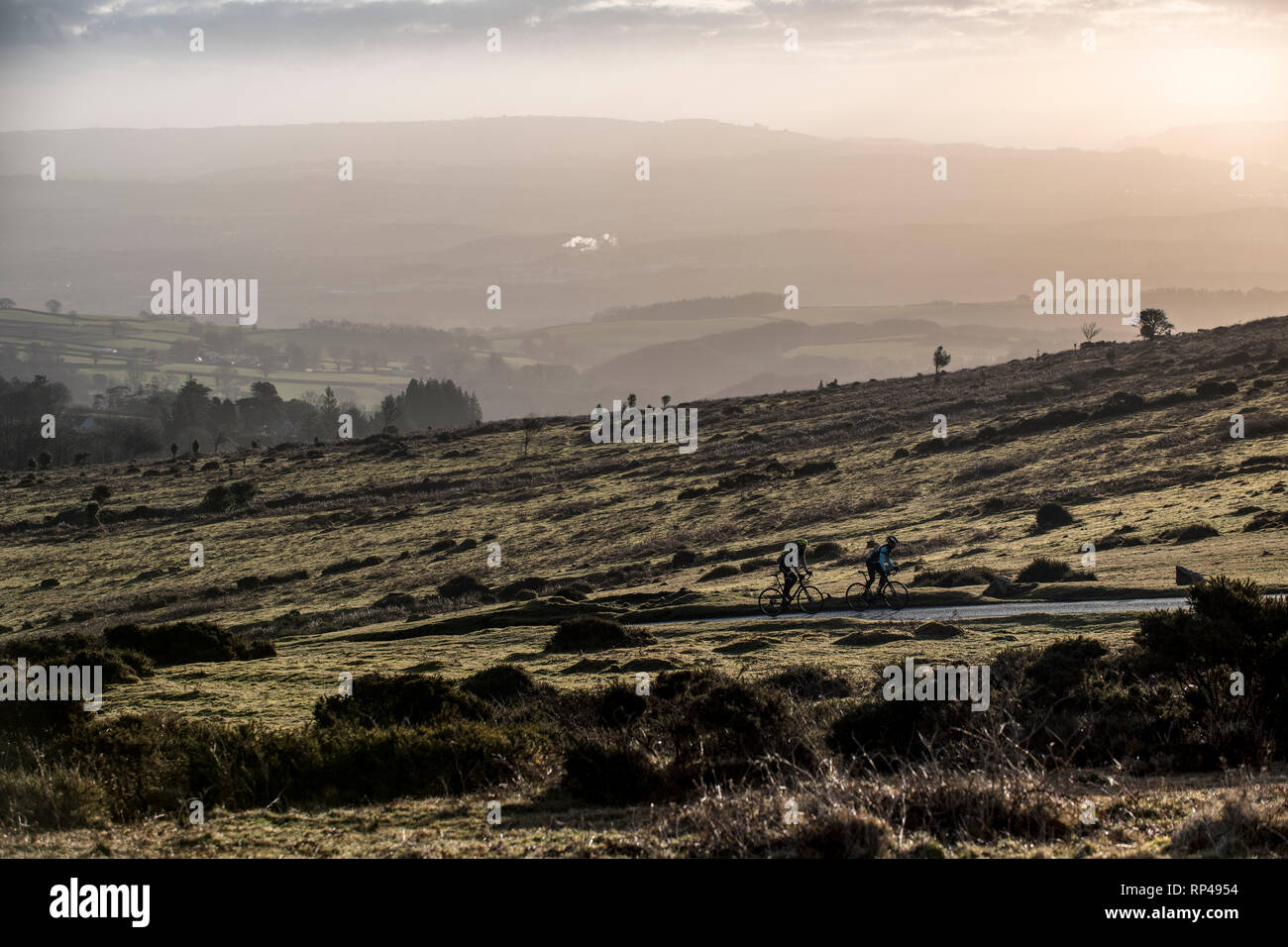 Due uomini corsa biciclette da strada fino alla cima di una collina vicino Haytor su Dartmoor nel Devon, Inghilterra all'alba. Foto Stock