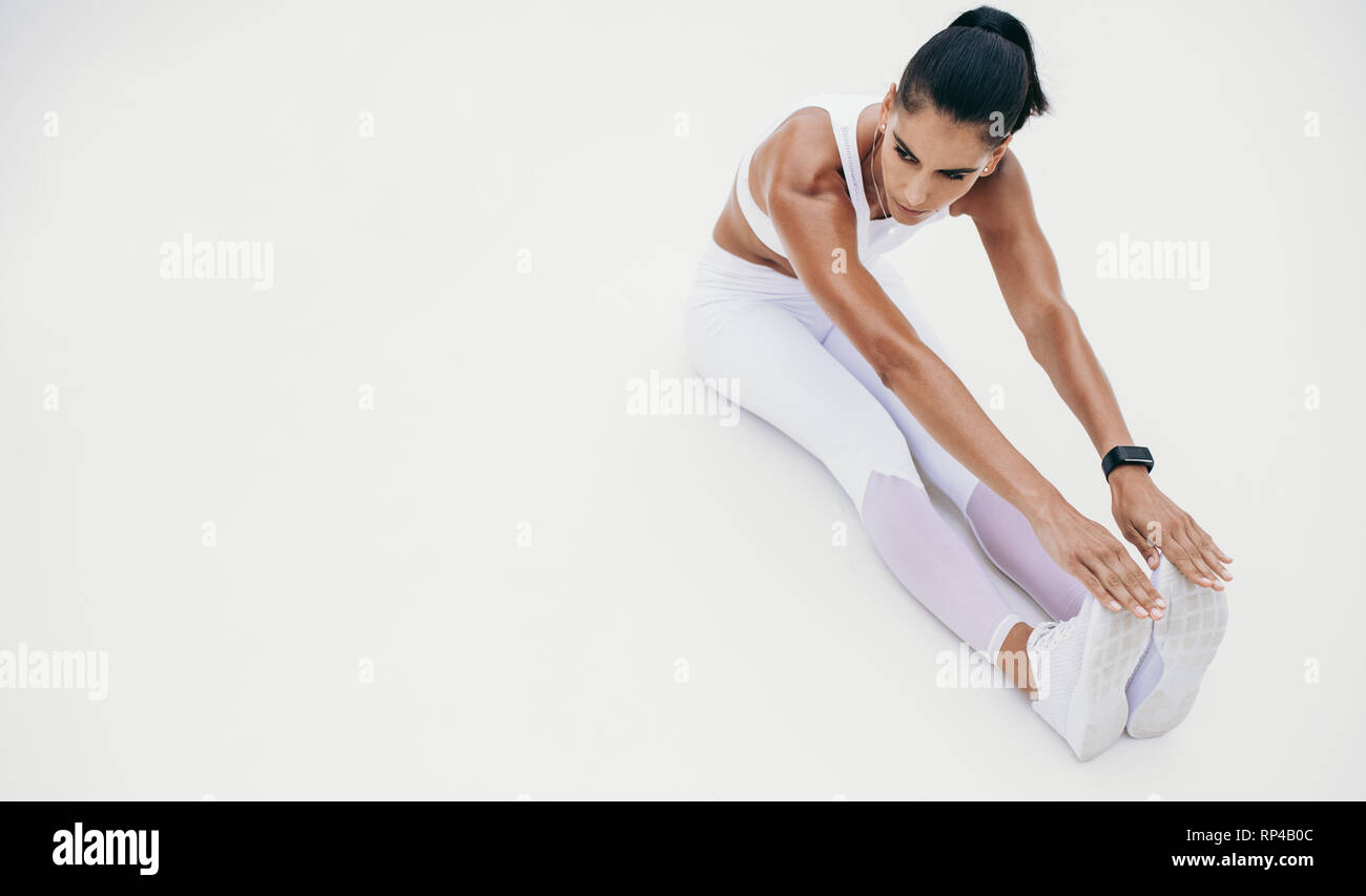 Vista dall'alto di una donna che si piega in avanti e tiene i piedi seduti sul pavimento. donna fitness che fa esercizi di stretching. Foto Stock