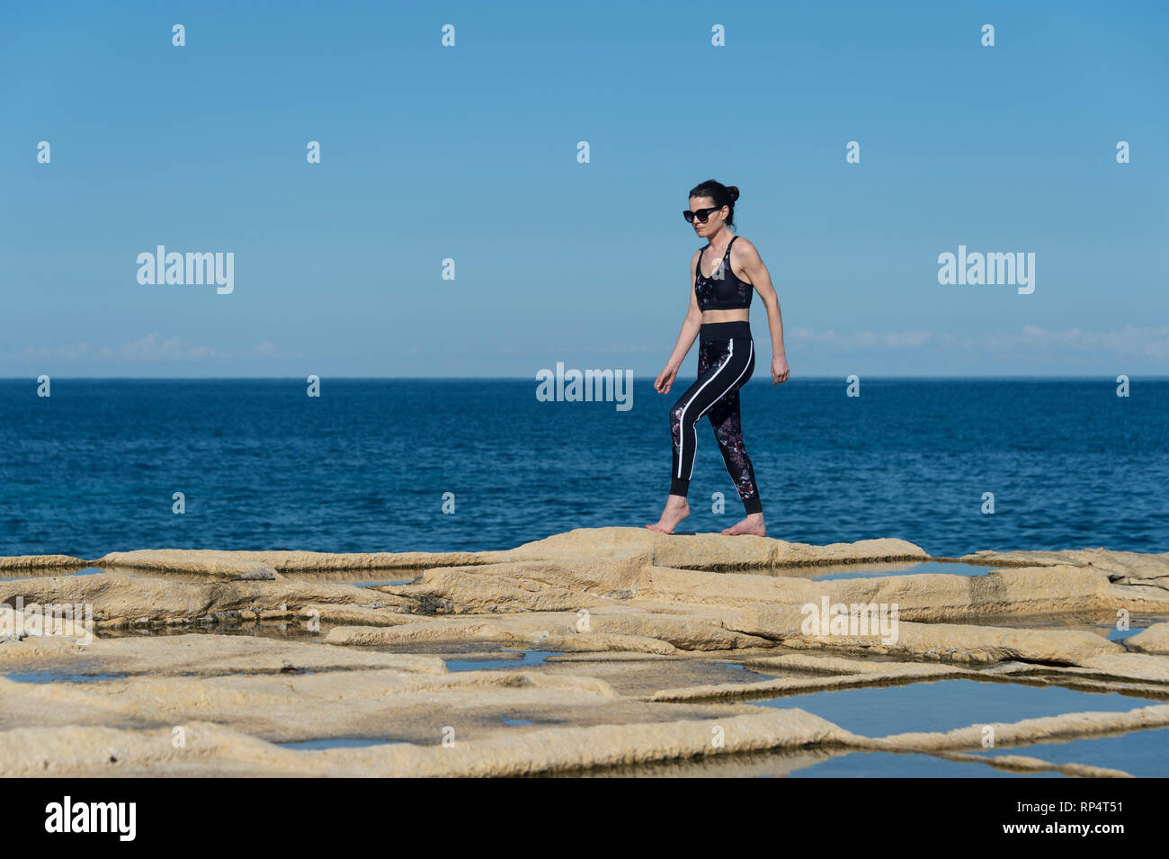 Donna che indossa abbigliamento sportivo a scavalcare rocce calcaree dal mare in malta Foto Stock