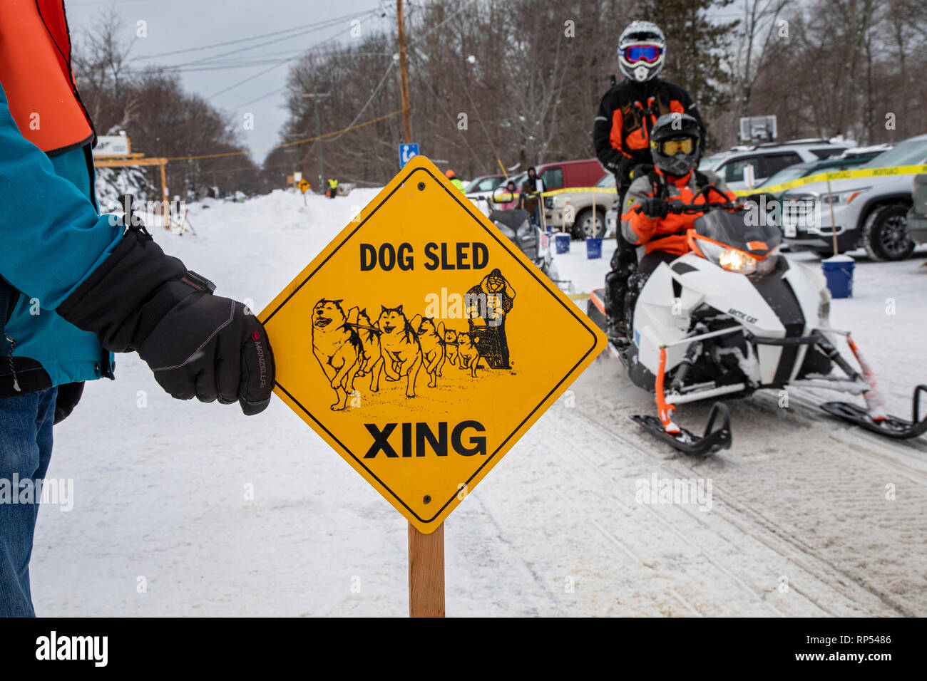 Grand Marais, Michigan - un attraversamento Guard si blocca il traffico su una motoslitta trail per consentire dogsled racers per passare. Essi sono al giro di boa della fino Foto Stock