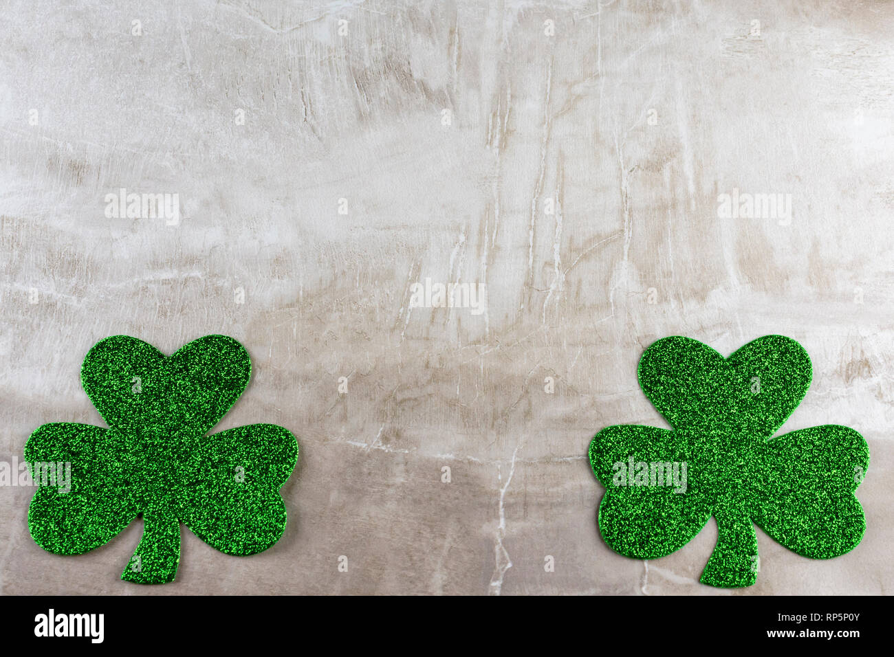 Due verdi glittery trifogli, uno in ogni angolo inferiore su un tan mattonelle in pietra. Abbondanza di spazio copia. Foto Stock