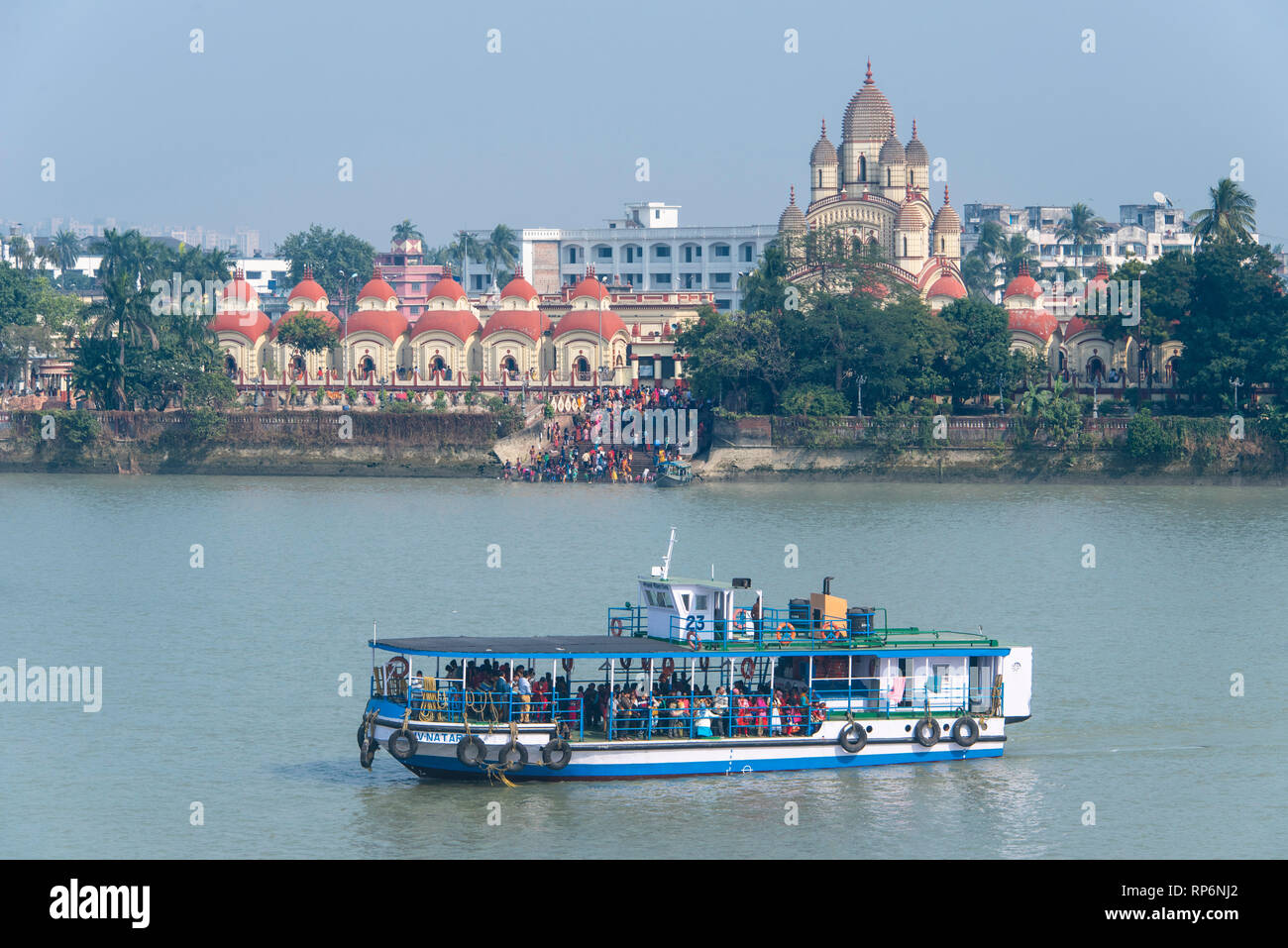 Il Dakshineswar Kali Temple Ghat sulle rive del Fiume Hooghly con la popolazione locale la balneazione e lavaggio e una barca in primo piano in una giornata di sole. Foto Stock