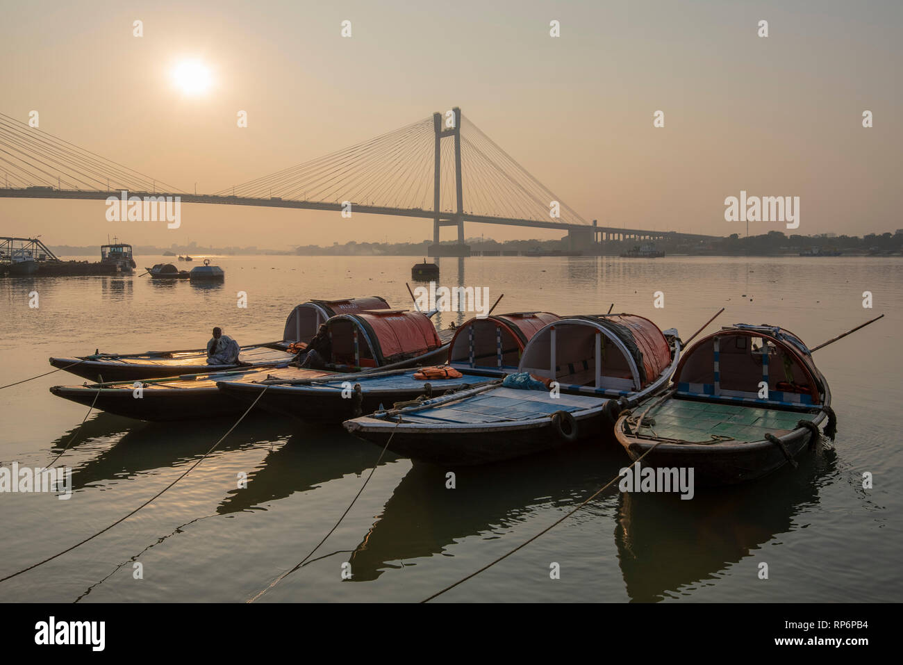 Un HDR vista del Vidyasagar Setu ponte presi da Prinsep Ghat sul Fiume Hooghly al tramonto con le imbarcazioni turistiche in primo piano in Kolkata. Foto Stock