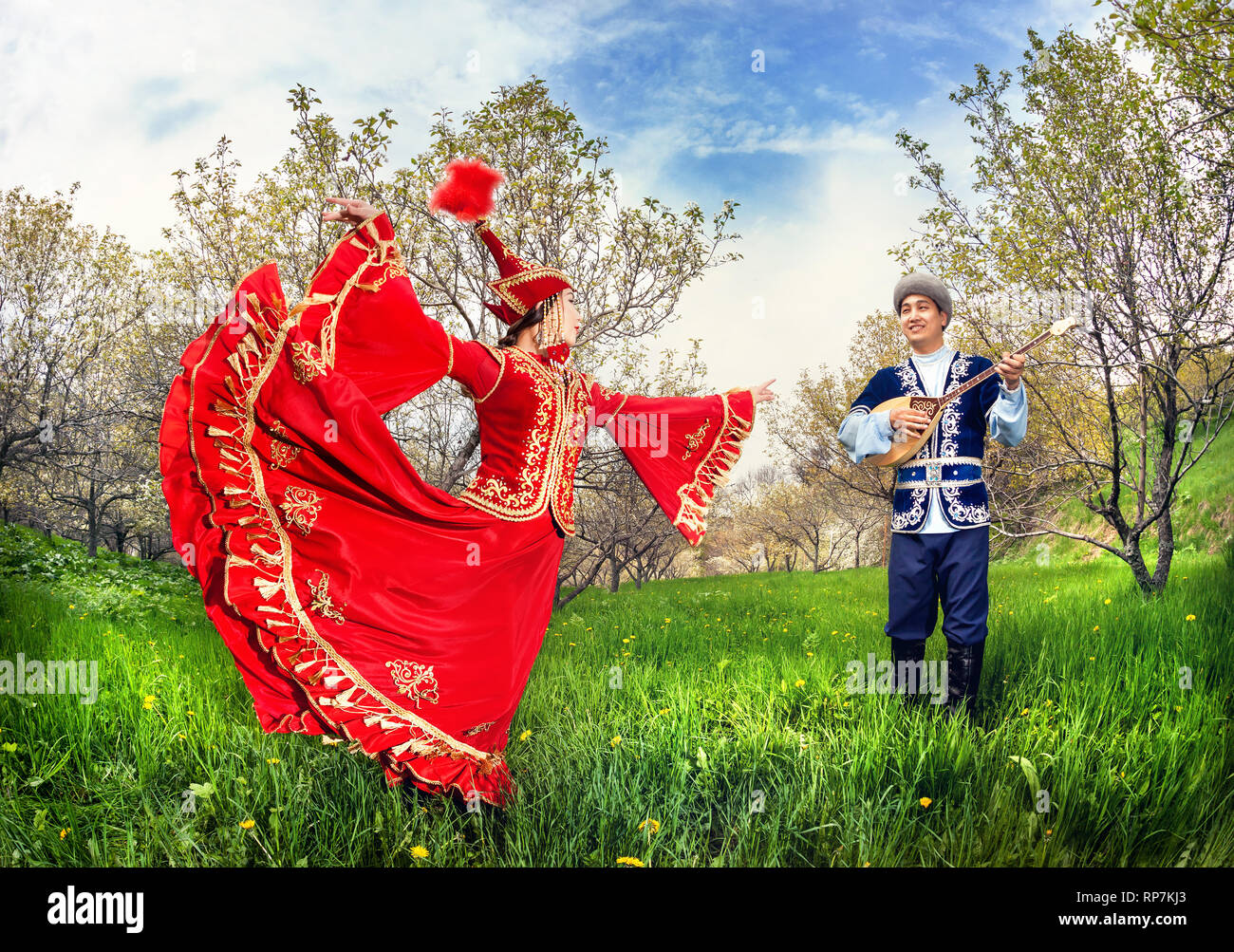 Il kazako woman dancing in abito rosso e uomo dombra giocando a fioritura primaverile giardino ad Almaty in Kazakistan e in Asia centrale Foto Stock