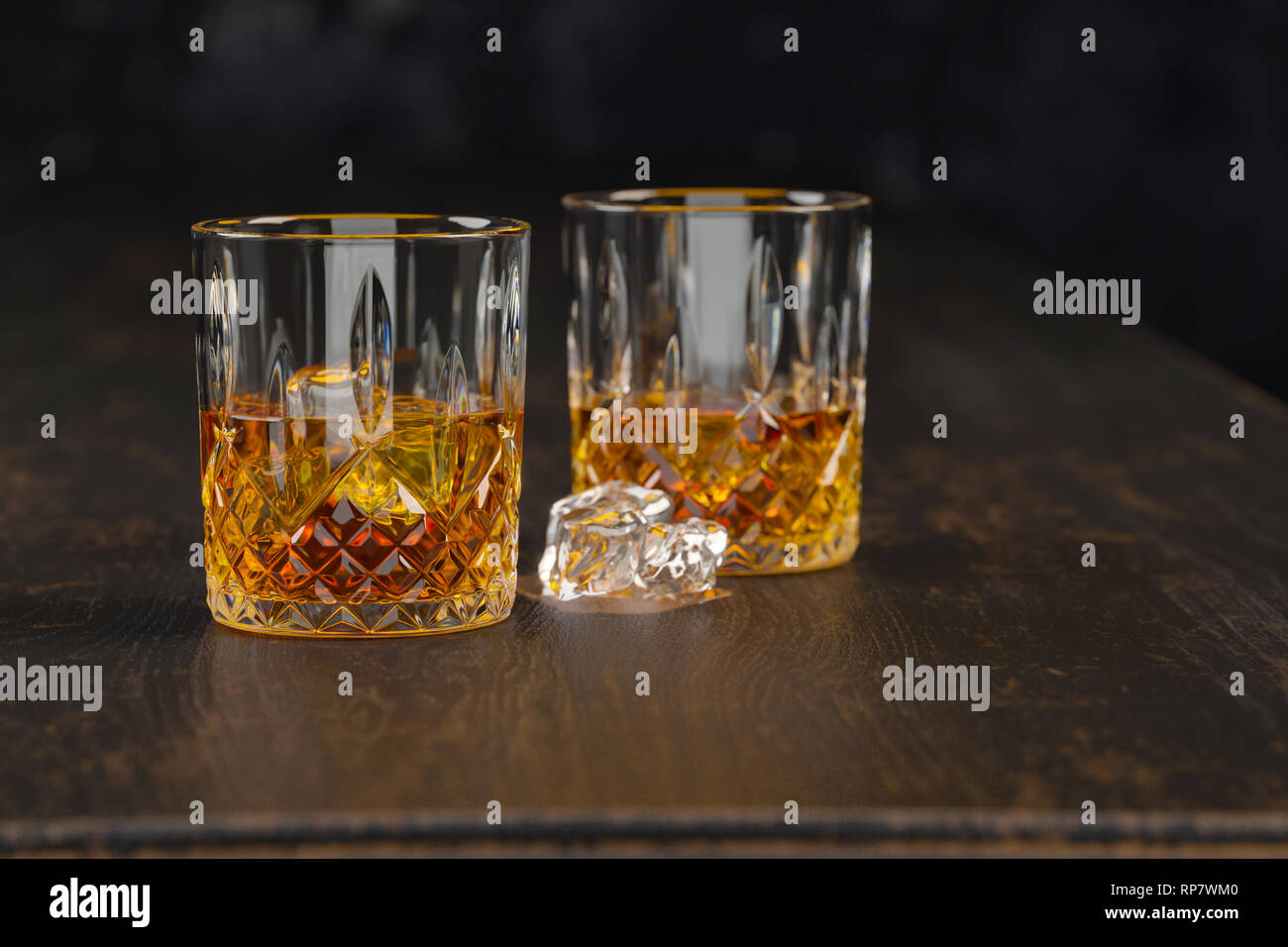 Whiskey due bicchieri con ghiaccio, stand al buio su un vecchio tavolo di legno su uno sfondo nero Foto Stock
