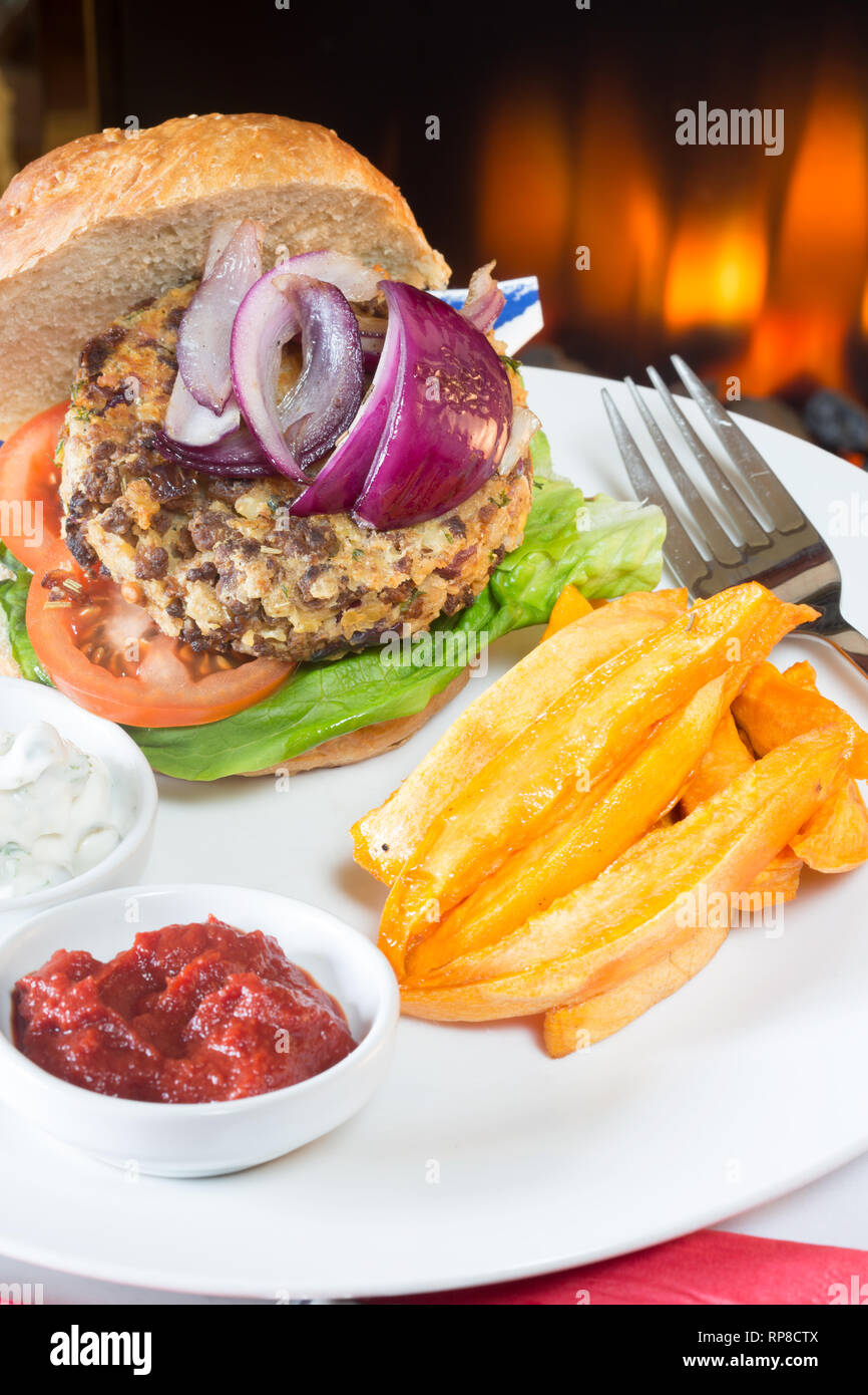 In casa di Quorn burger in un panino a lievitazione naturale con lattuga, pomodoro, cipolla rossa, patata dolce chip/patatine fritte, e servita con ketchup e yogurt di soia salse. Foto Stock